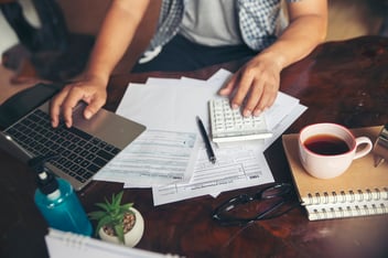 A person managing their finances on a laptop at home with a budgeting app open on the screen, surrounded by papers and a calendar. The atmosphere is modern and well-lit, suggesting a sense of organization and control. A piggy bank and coffee cup are nearby, symbolizing savings and comfort